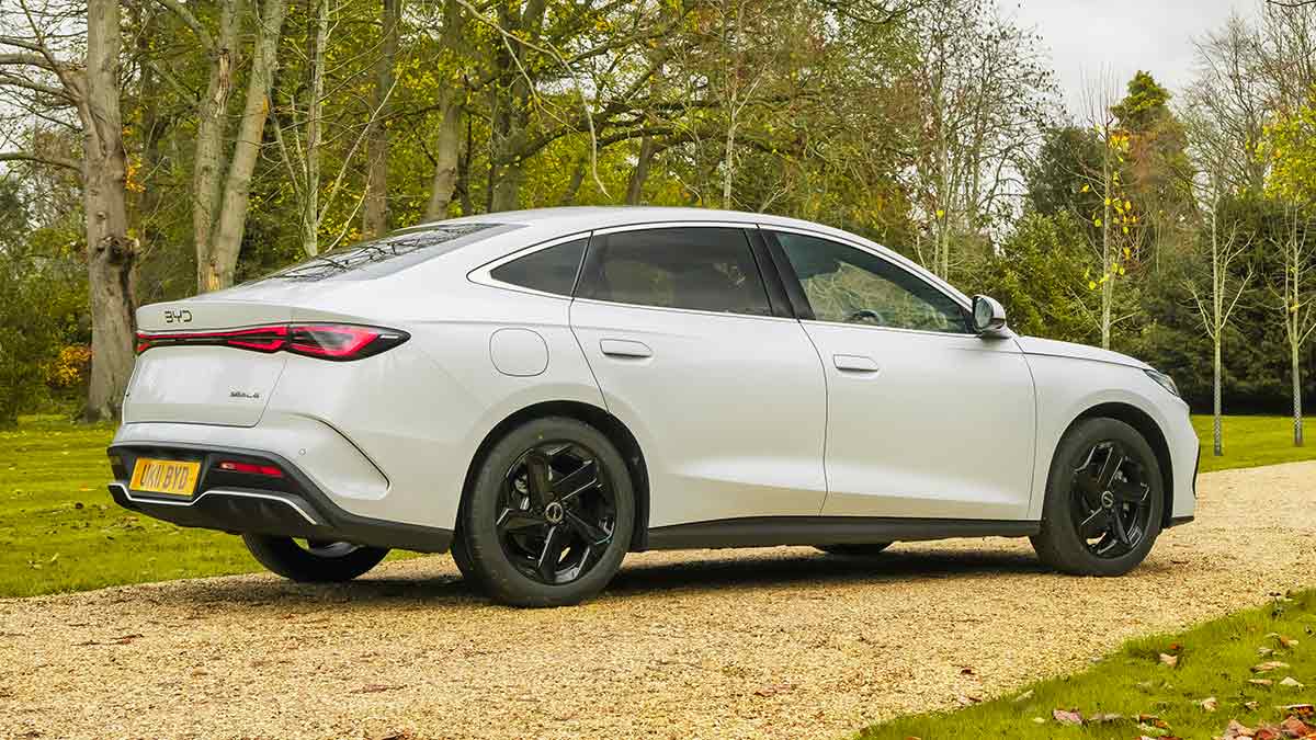 Rear view of white BYD Seal 6 sedan on stone driveway of leafy country estate in England.