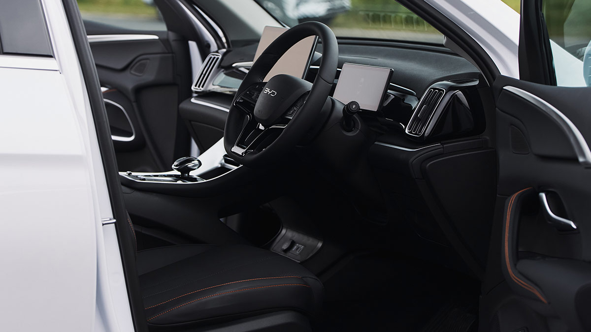 Look inside BYD Sealion 5 SUV cockpit from driver's door, showing dark synthetic leather trim, red stitching, dual digital screens.
