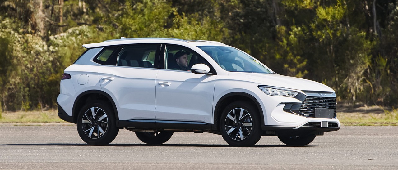 White BYD Sealion 5 SUV on bitumen concourse at Lang Lang proving ground in Victoria with thick shrub and gum trees behind.