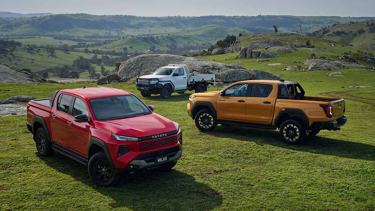 Red Toyota HiLux Rogue, gold HiLux SR5 and white single cab-chassis model on rocky, open ridge with mountain range behind.
