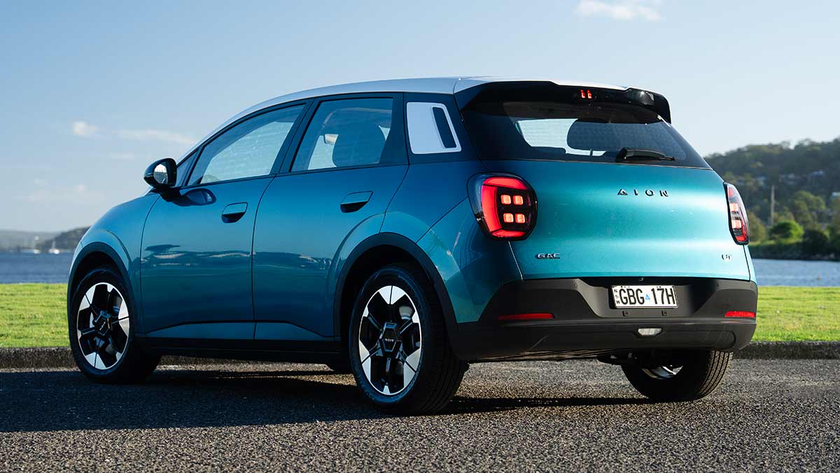 Rear view of green GAC Aion UT electric hatch at waterfront carpark with boats on bay in background.
