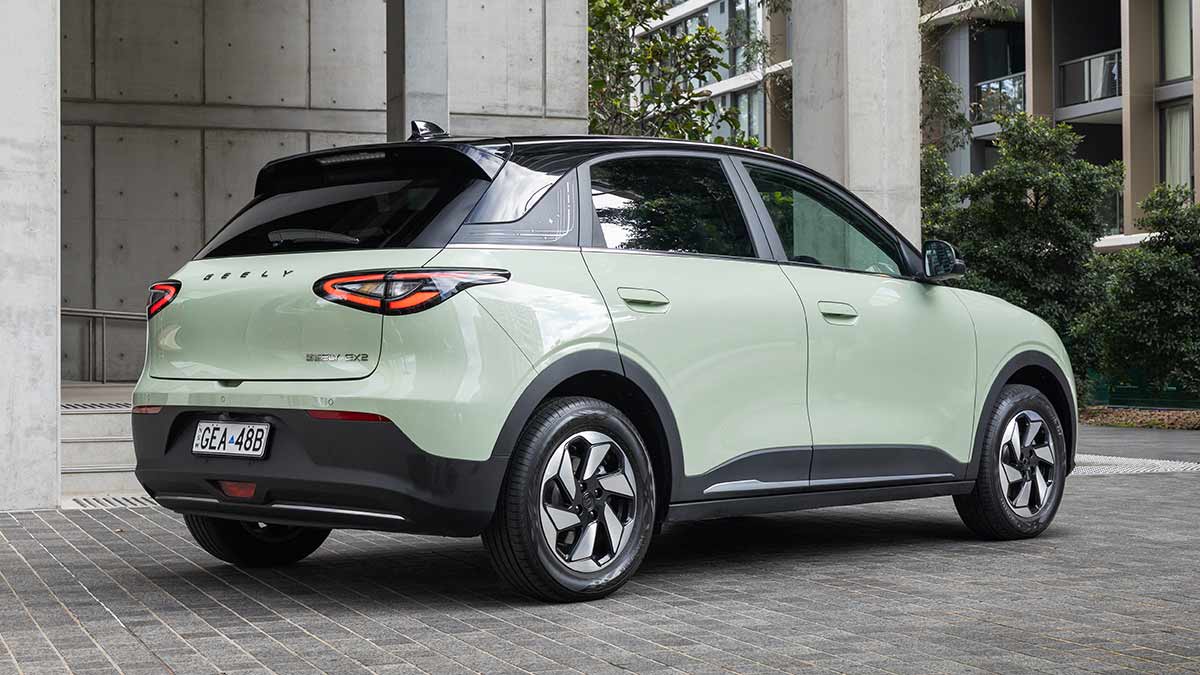 Rear view of light green Geely EX2 electric hatch with black roof, parked outside city building with thick concrete pillars.