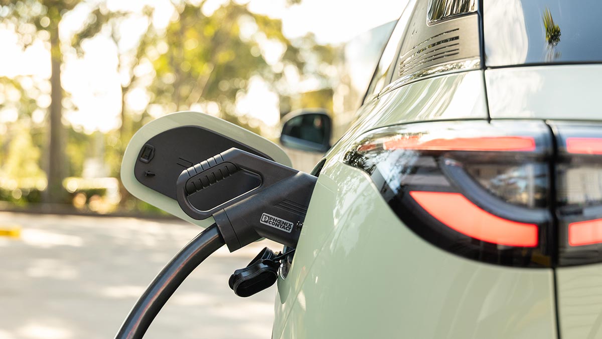 Rear close-up shot of light green Geely EX2 electric hatch with black DC fast-charging cord plugged into socket at side of car.