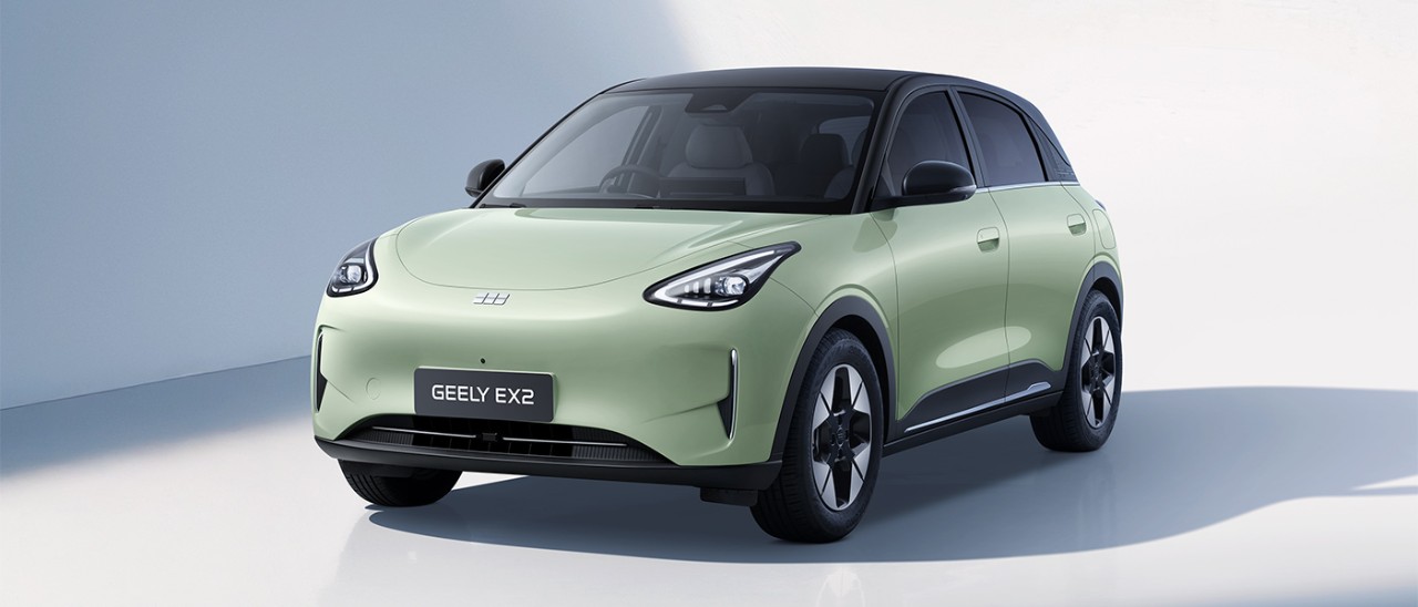 Frontal studio shot of pistachio green Geely EX2 electric city car with black roof and cloverleaf design alloy wheels.