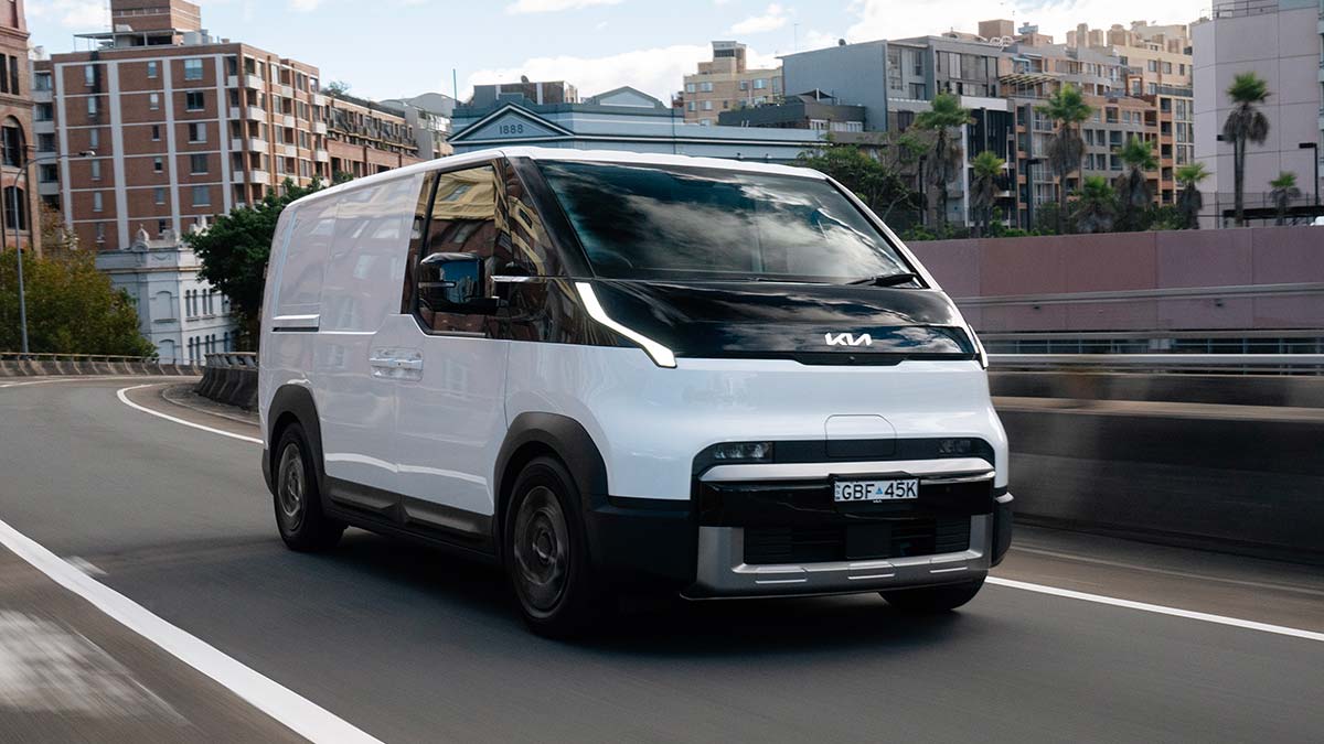 White Kia PV5 electric van on Sydney arterial road surrounded by large buildings.