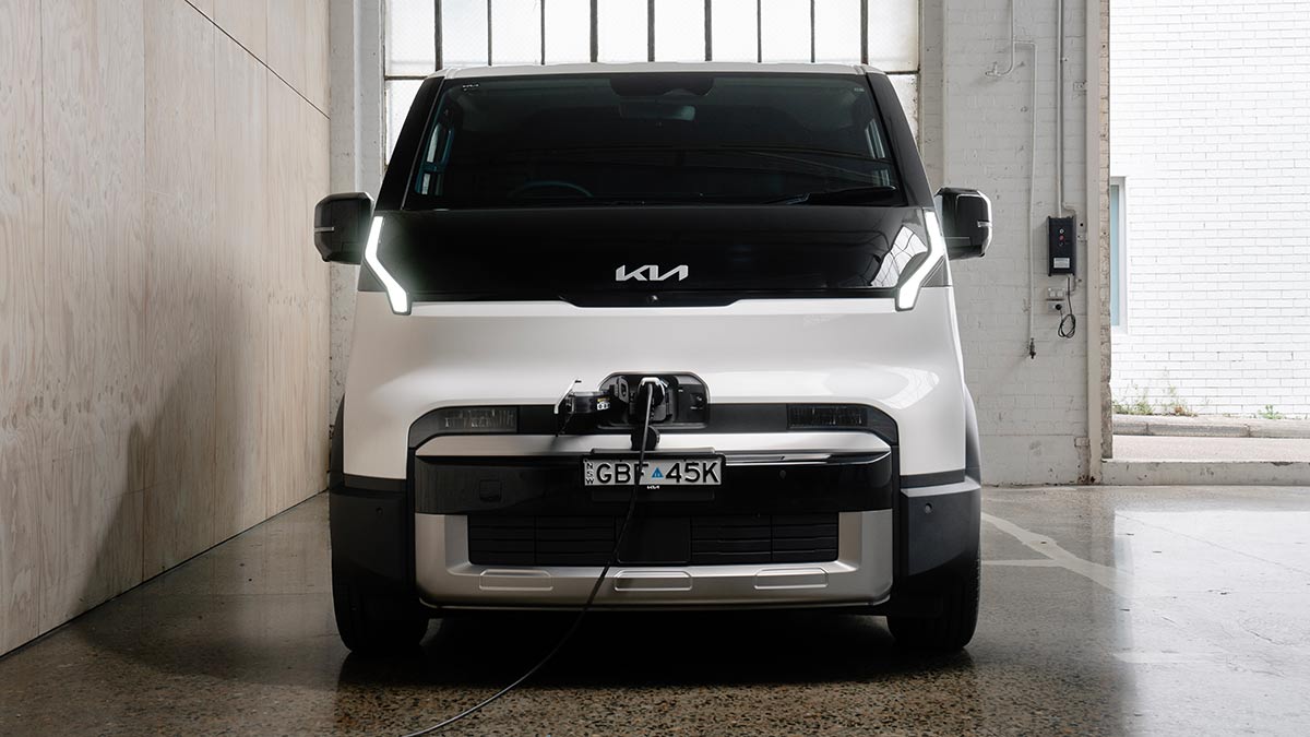 White Kia PV5 Cargo parked in warehouse with EV charging cord attached to port at front of van.