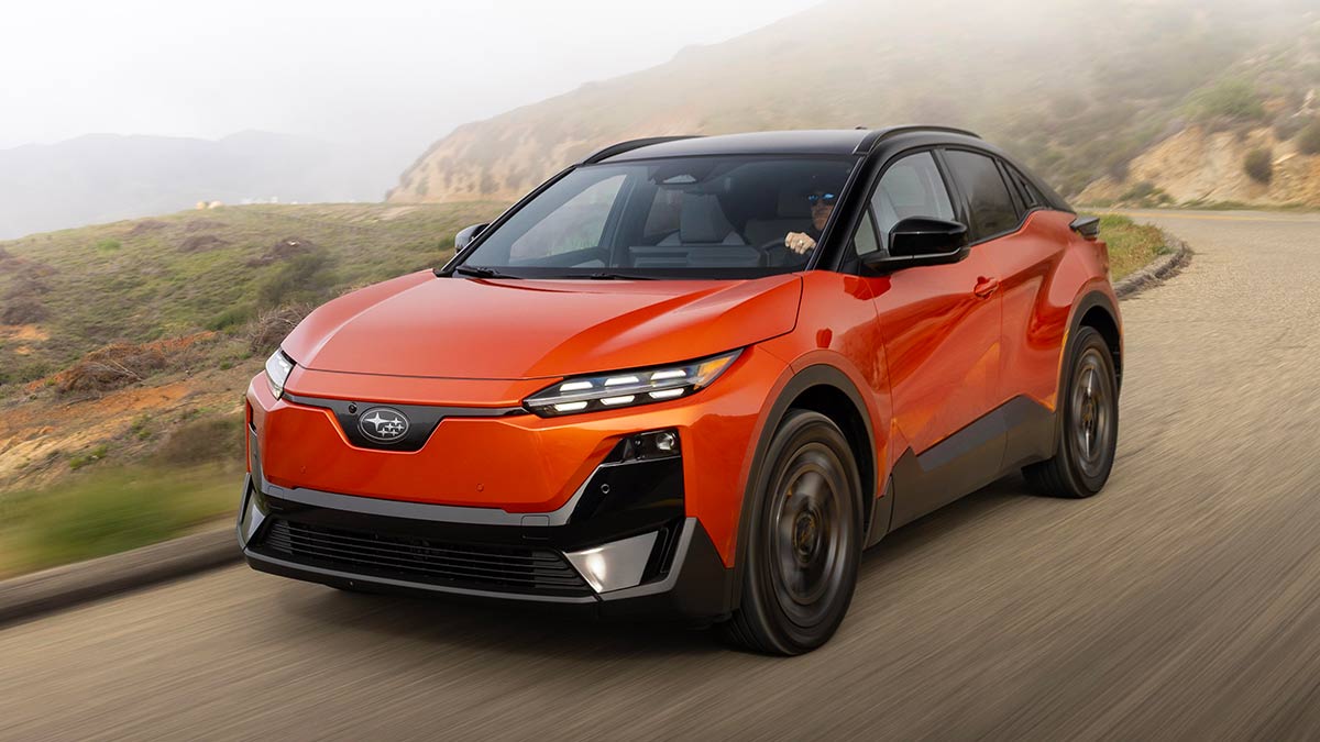 Left-hand-drive US-spec orange metallic Subaru Uncharted small electric SUV driving on alpine road in misty conditions.
