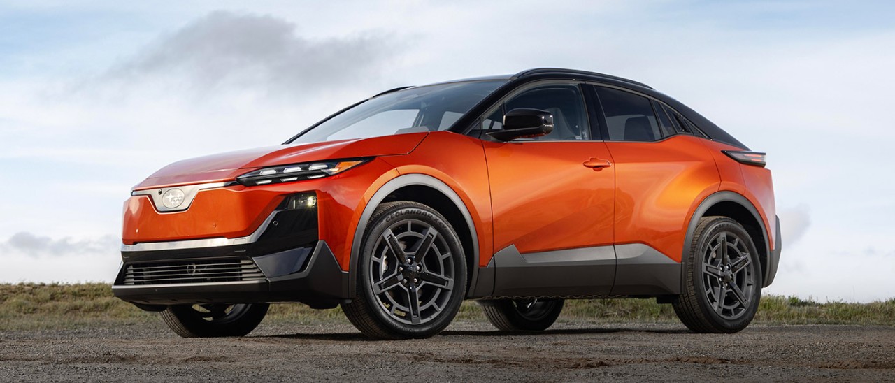 Orange metallic Subaru Uncharted small electric SUV parked on gravel road with skyline in background.