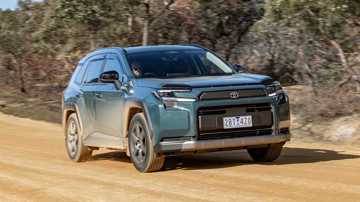 Metallic green Toyota RAV4 Edge SUV driving on wide dirt road with light brown mud on side of car. 