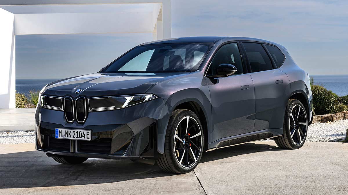 Blue BMW iX3 SUV in left-hand drive parked in front of white luxury house overlooking sea.