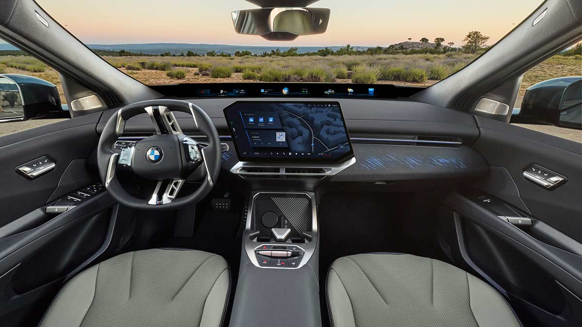 BMW iX4 cockpit with large centre screen, full-width secondary screen below windscreen, agave green upholstery and dark grey dash trim. 