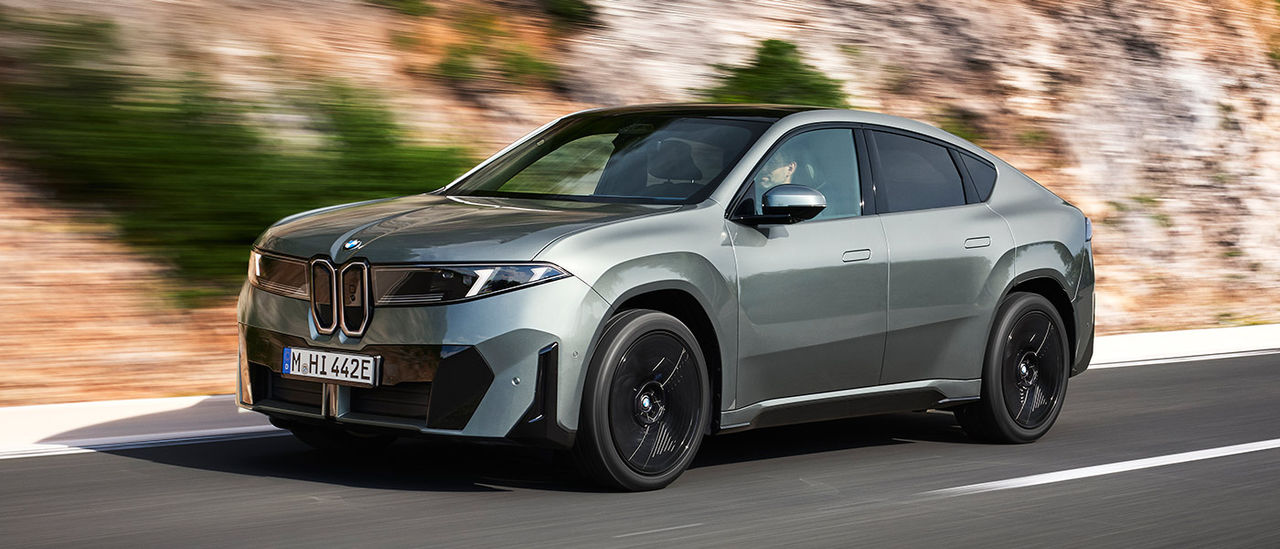 Metallic sage green BMW iX4 50 xDrive coupe-style SUV in left-hand-drive on high-banked coastal road in Europe.