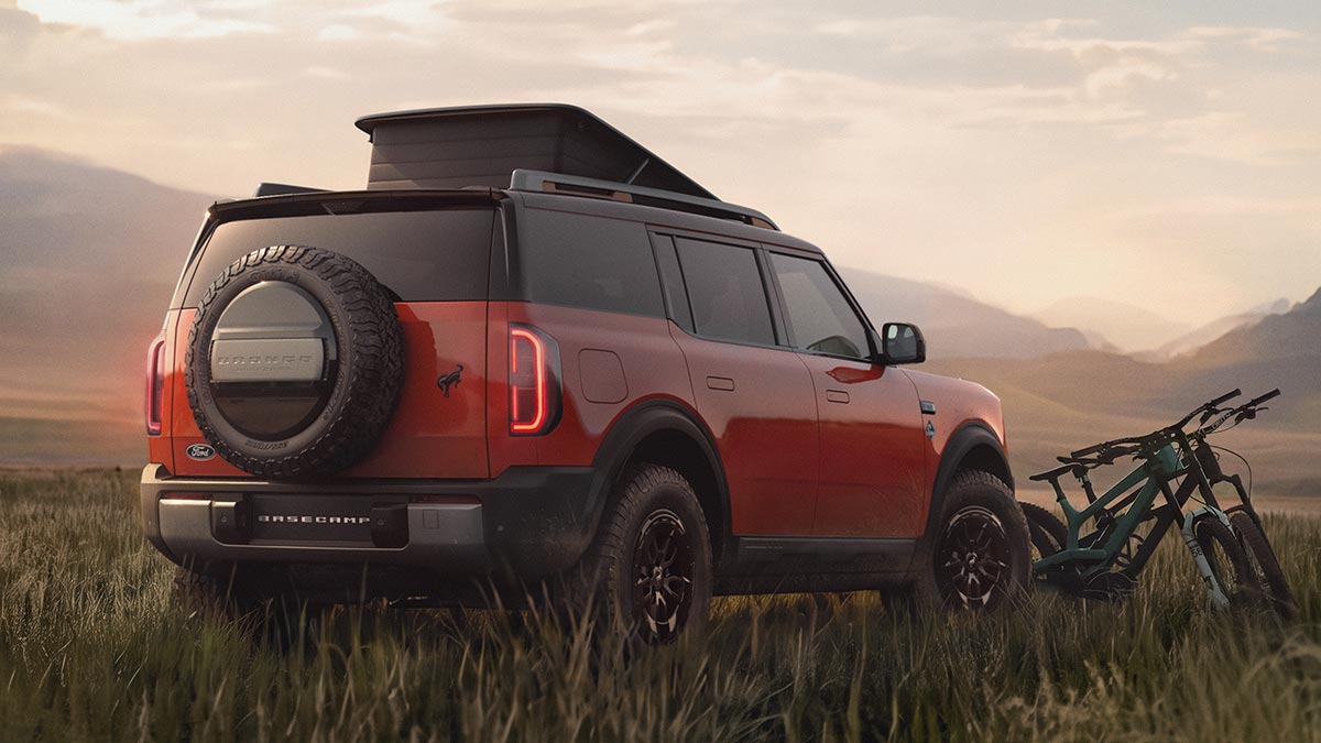 Rear view of red Ford Bronco Basecamp SUV in high country camping spot with pop-top roof raised and mountain bikes next to vehicle.
