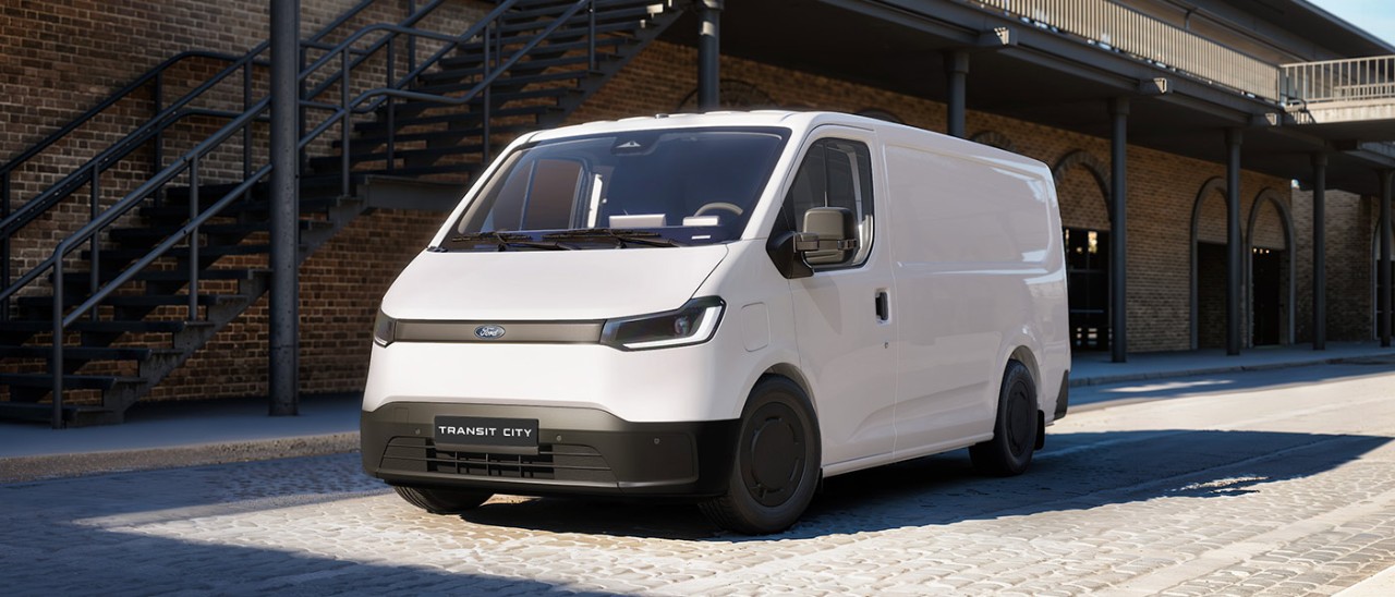 White European-spec Ford Transit City electric van parked on brick-paved forecourt of double-storey heritage industrial building.