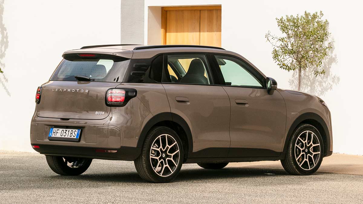 Rear view of light brown Leapmotor B03X small electric SUV parked outside Tuscan villa with olive tree against white wall.