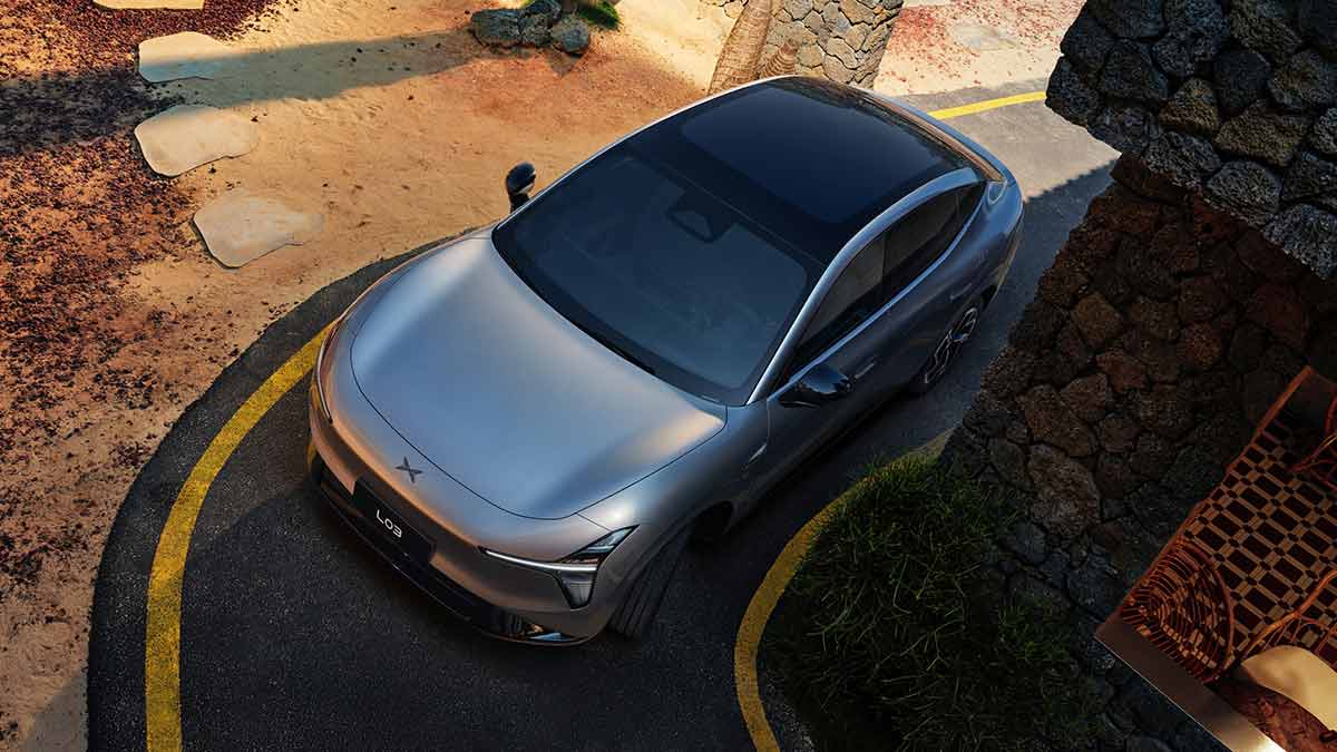 Overhead shot of light grey XPeng L03 SUV taking corner in tight narrow laneway next to stone building.