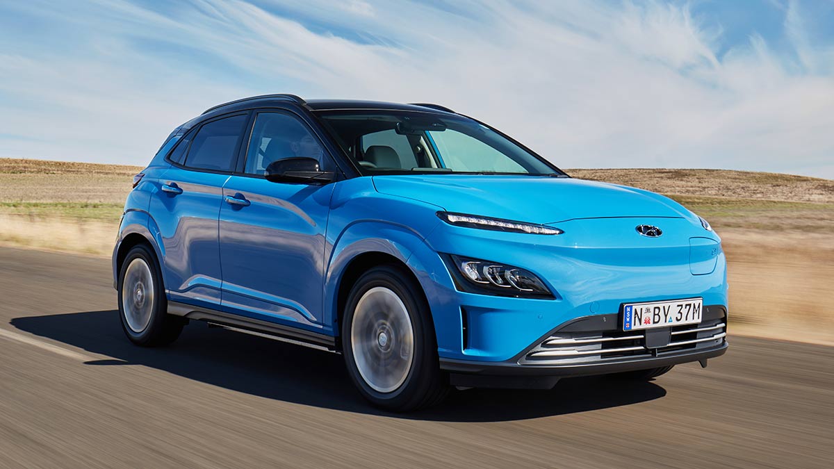 Bright blue 2021 Hyundai Kona Electric small SUV driving on road in barren landscape with big blue sky.