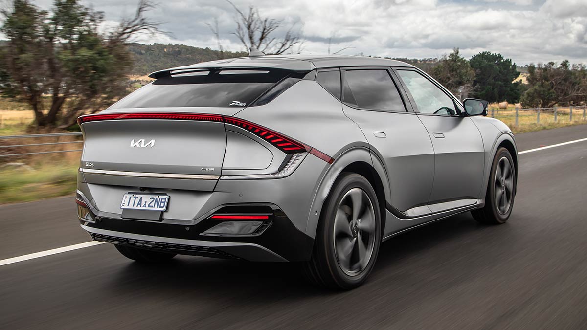 Rear view of metallic grey 2022 Kia EV6 SUV on rural Victorian highway with wire rope barrier and sparse trees bordering hay paddocks.