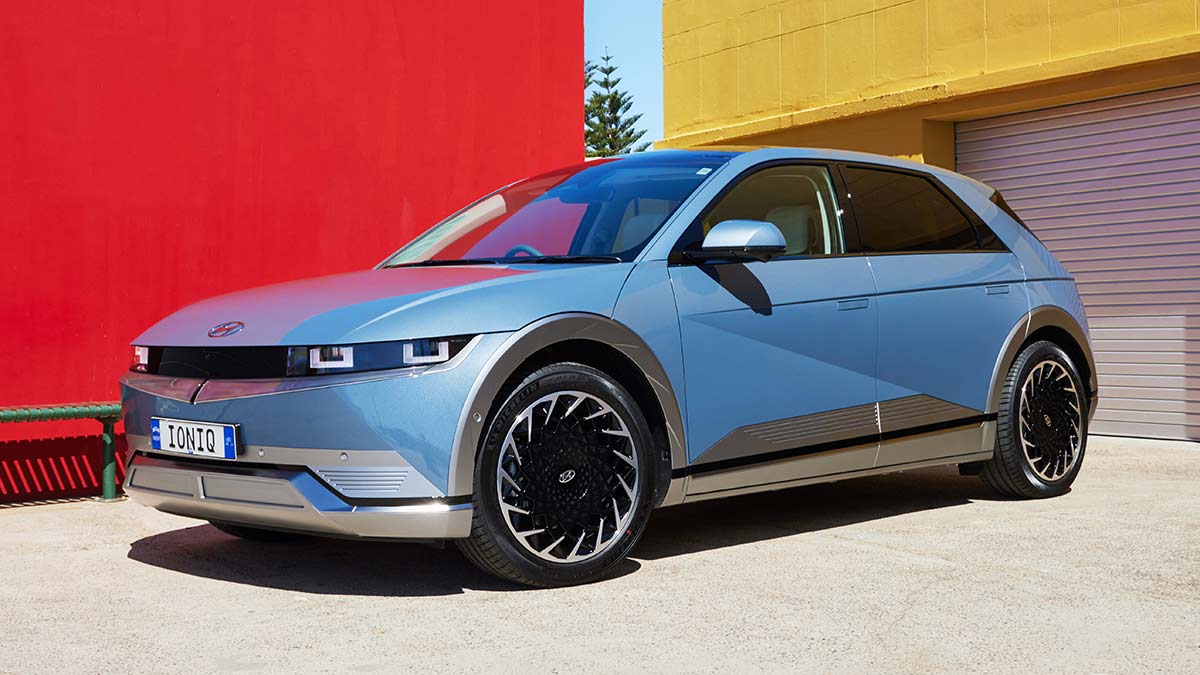 Metallic blue 2021 Hyundai Ioniq 5 mid-size electric SUV parked in front of bright red and yellow buildings.