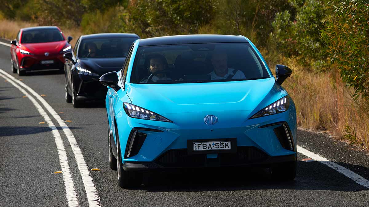 Bright blue MG4 electric hatch on tree-lined country road followed by black and red MG4 EVs behind.