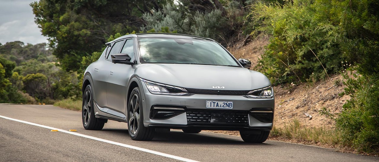 Metallic grey 2022 Kia EV6 SUV on winding Victorian coastal road with high sandy banks and tea trees.