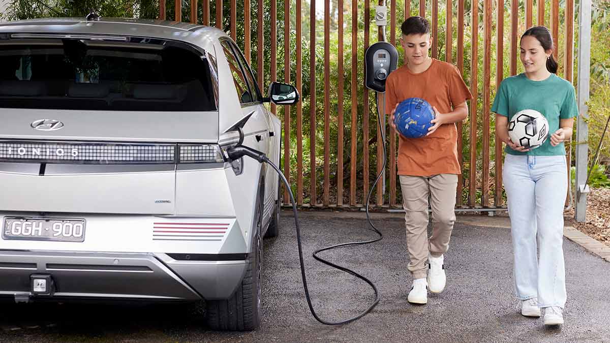 Boy and girl holding soccer balls in carport next to white Hyundai Ioniq 5 EV being charged with home EV charger
