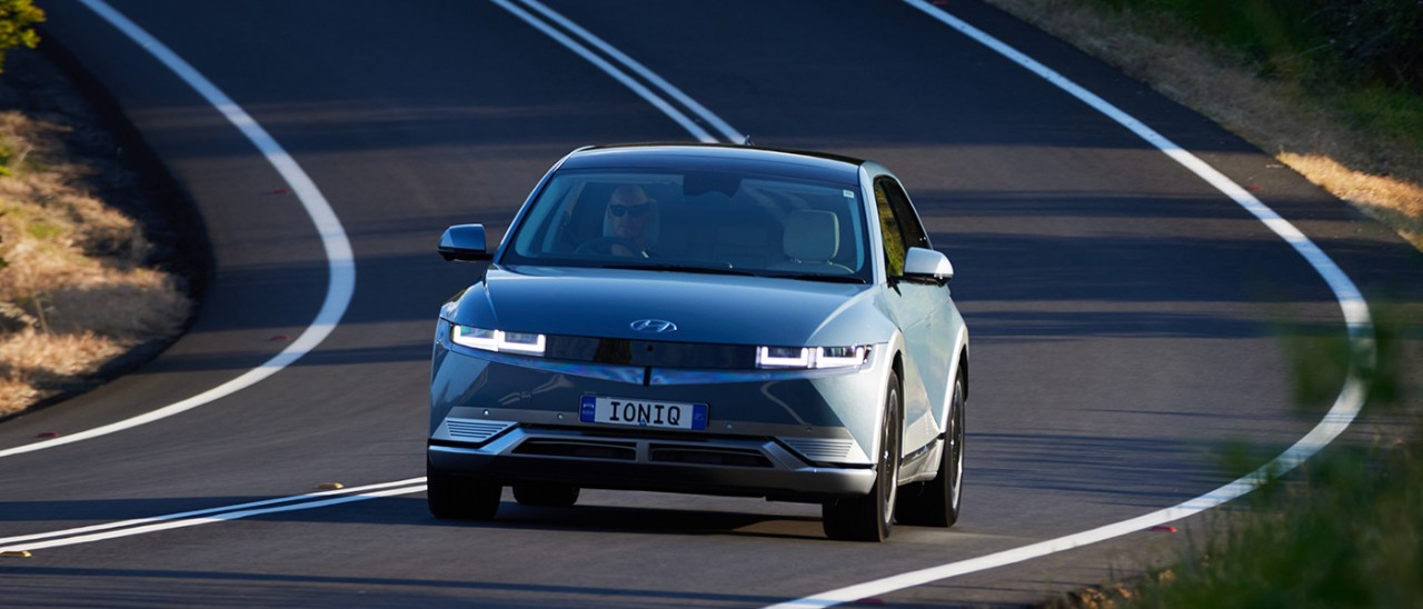 2022-Hyundai-Ioniq-5-front-action-banner-1400x600 Frontal shot of blue Hyundai Ioniq 5 electric car on downhill corner of country road