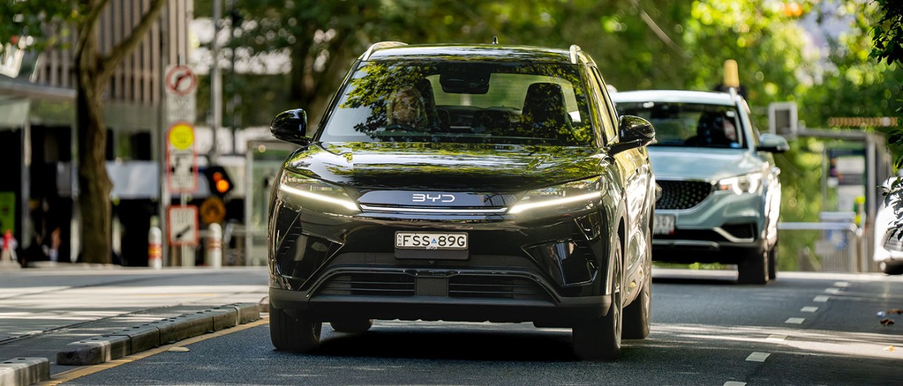 Black BYD Atto 2 electric small SUV driving on leafy street next to tram lines in Melbourne CBD.