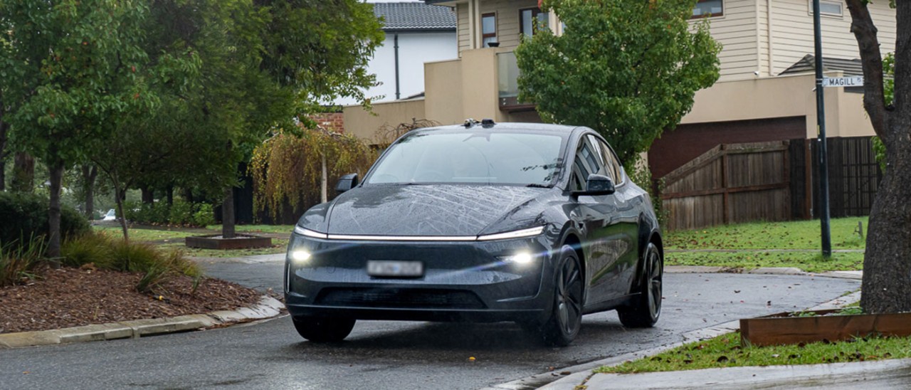 Modified dark blue Tesla Model Y EV driving on wet and leafy Geelong suburban street in real-world range and efficiency testing program.