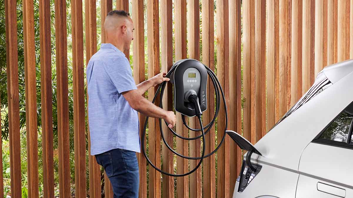 Man in blue shirt in carport getting connector from home EV charger on wall for white Hyundai Ioniq 5 EV in foreground