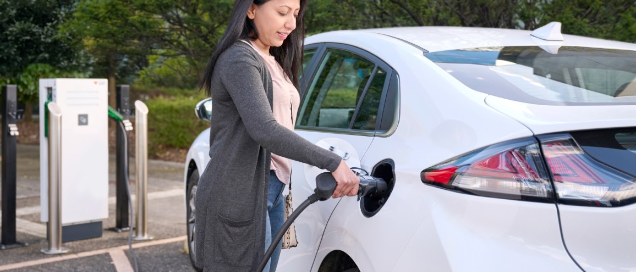 A woman her white EV at a public EV charger