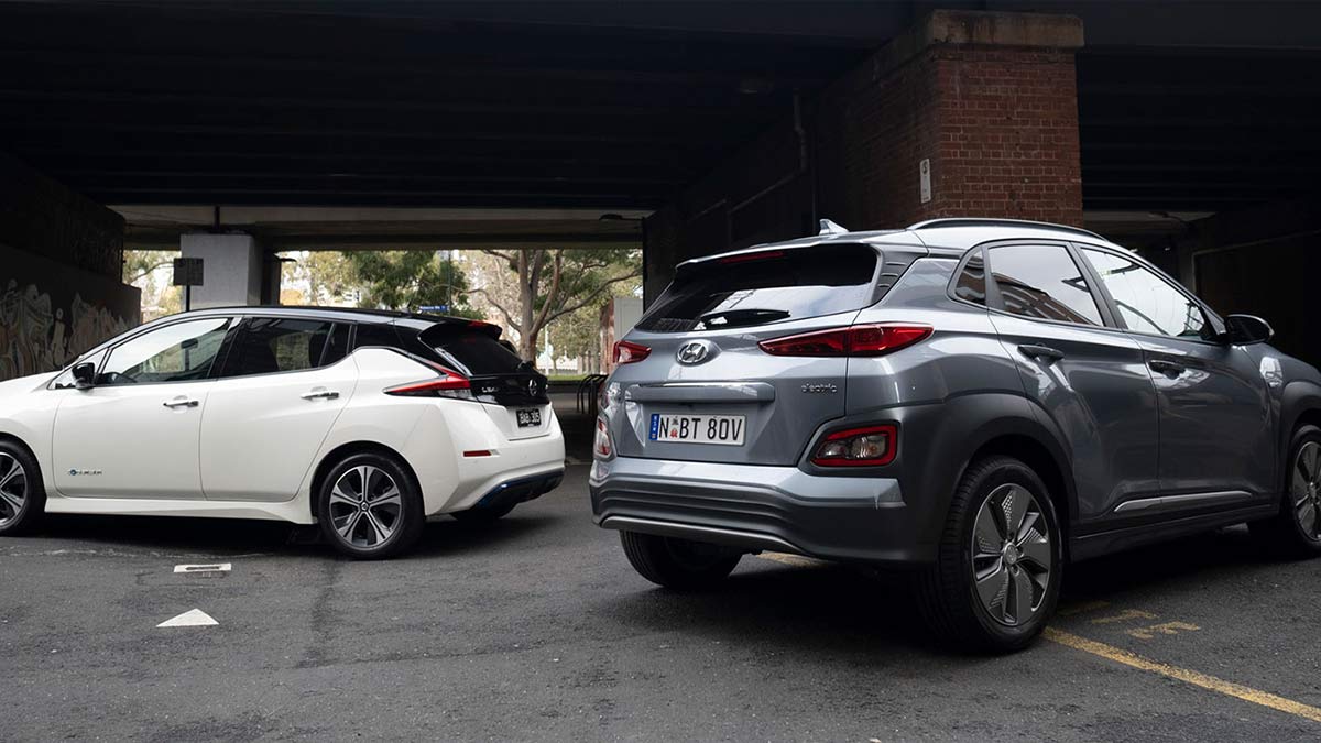 Rear side view of a white Nissan Leaf parked under a bridge next to a dark grey Hyundai Kona Electric Highlander