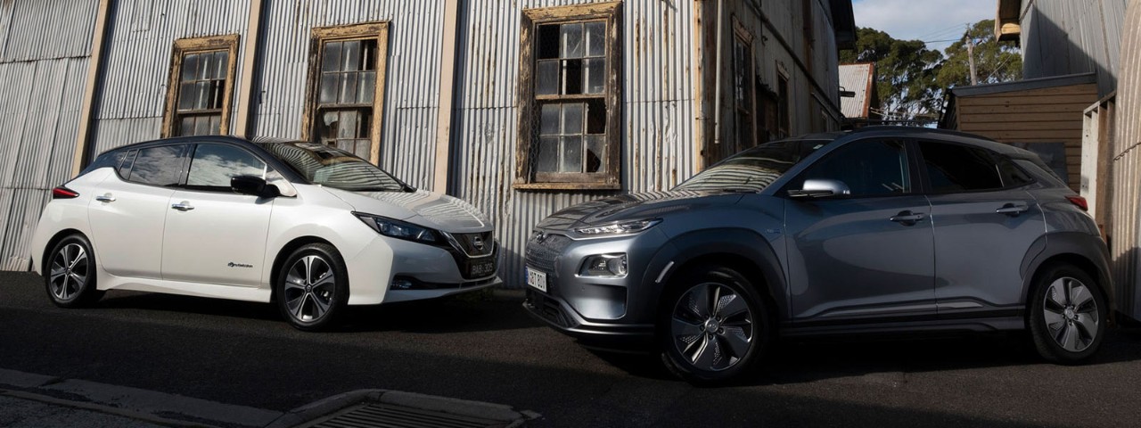 Front side view of a white Nissan Leaf parked next to a dark grey Hyundai Kona Electric Highlander