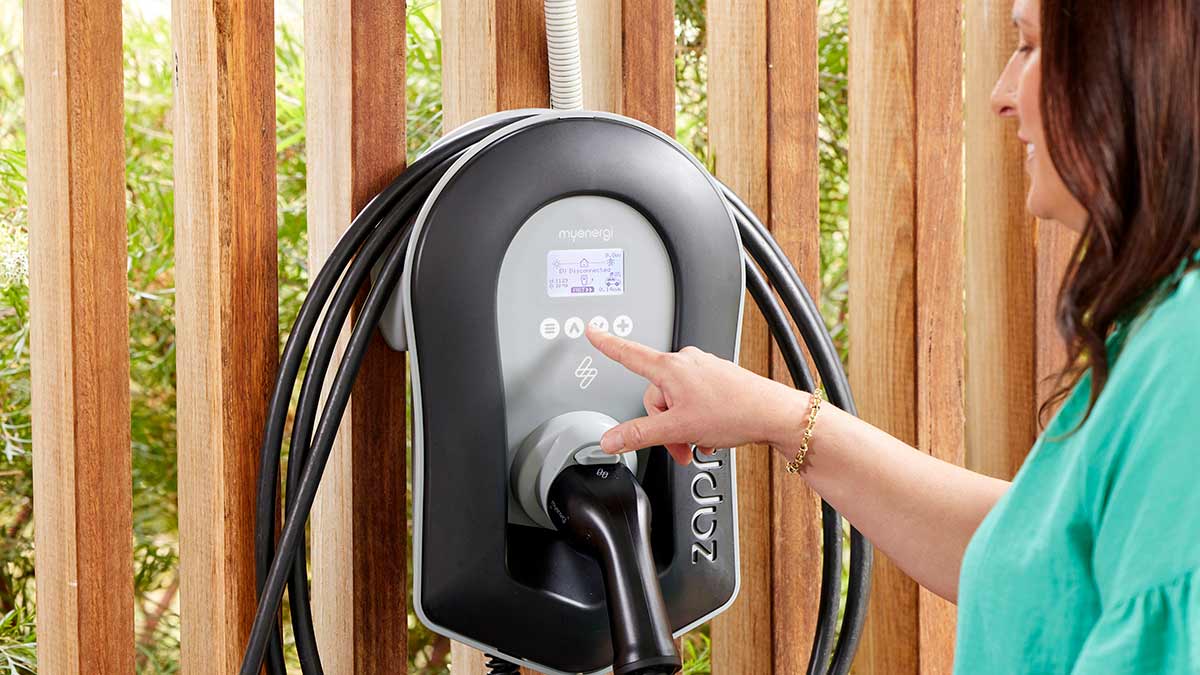 Woman with brown hair and green shirt pressing buttons on wall-mounted home EV charger in carport