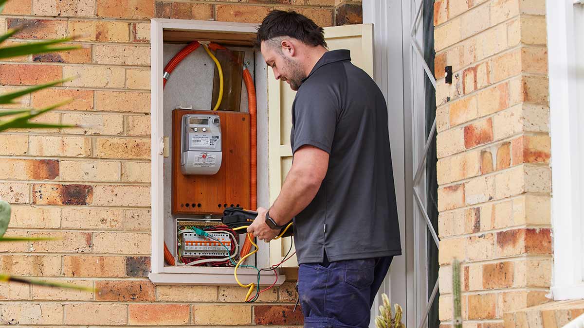 RACV electrician working on switchboard outside front door of cream brick house