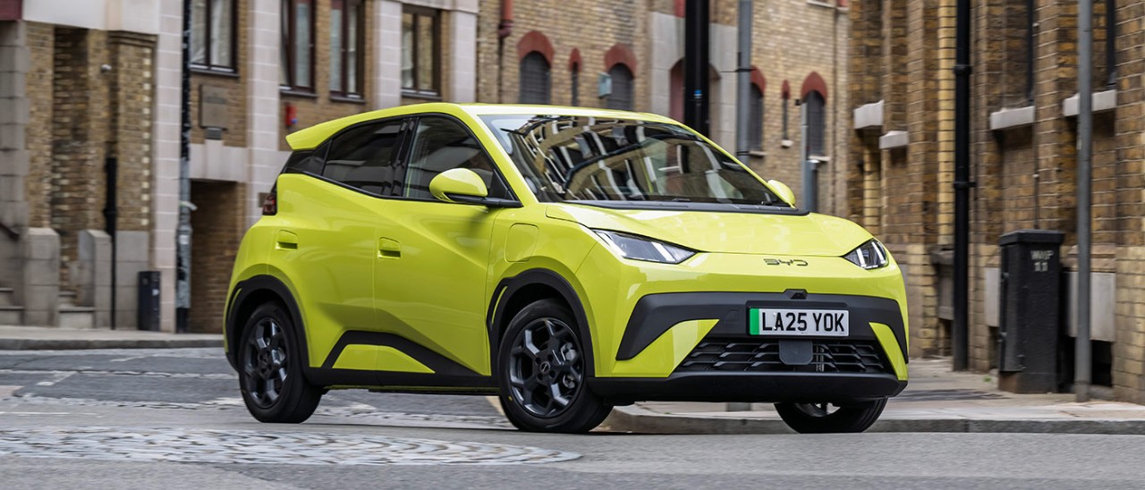Lime green BYD Atto 1 EV hatch in UK city street surrounded by brown brick buildings.