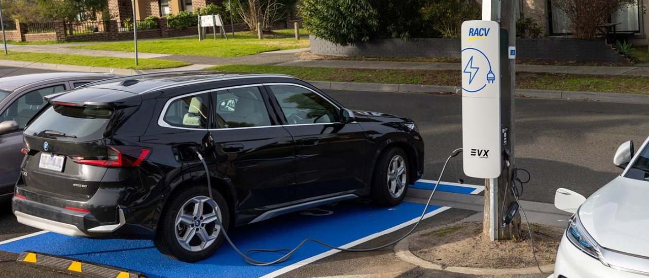 A black electric vehicle is parked at the kerb and connected to an EVX pole-mounted charger.