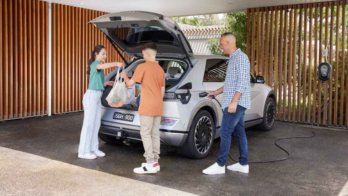 father plugging EV in at home while his children unpack groceries from car