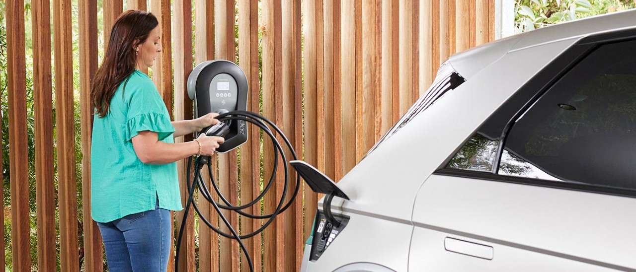 Woman getting EV charging cable from wall installation.