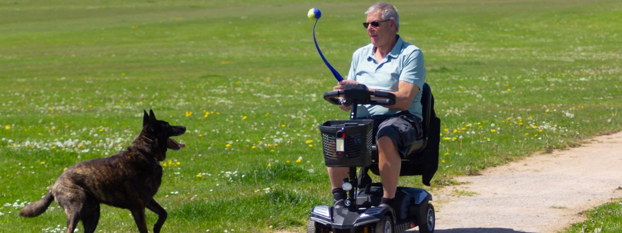 Man on mobility scooter taking dog for a walk