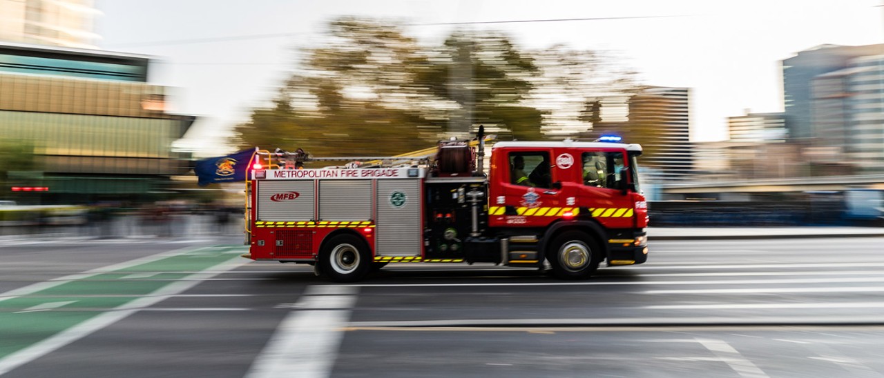 A red fire truck with flashing lights driving along a road in Melbourne