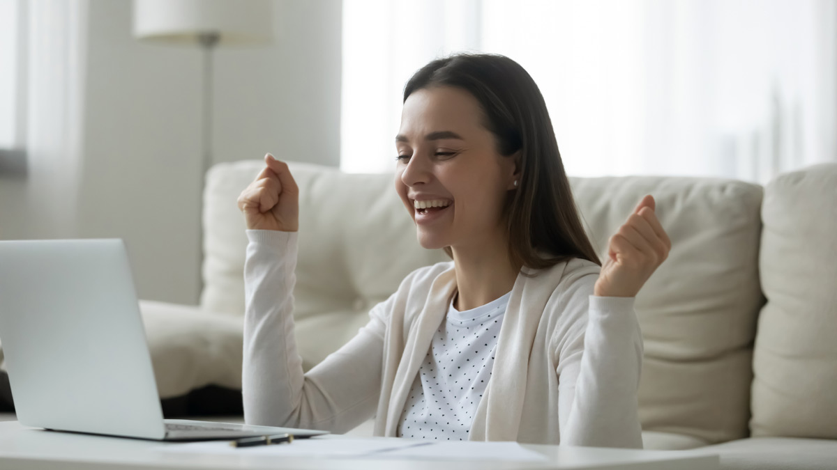 Girl sitting in front of laptop celebrates passing exam.