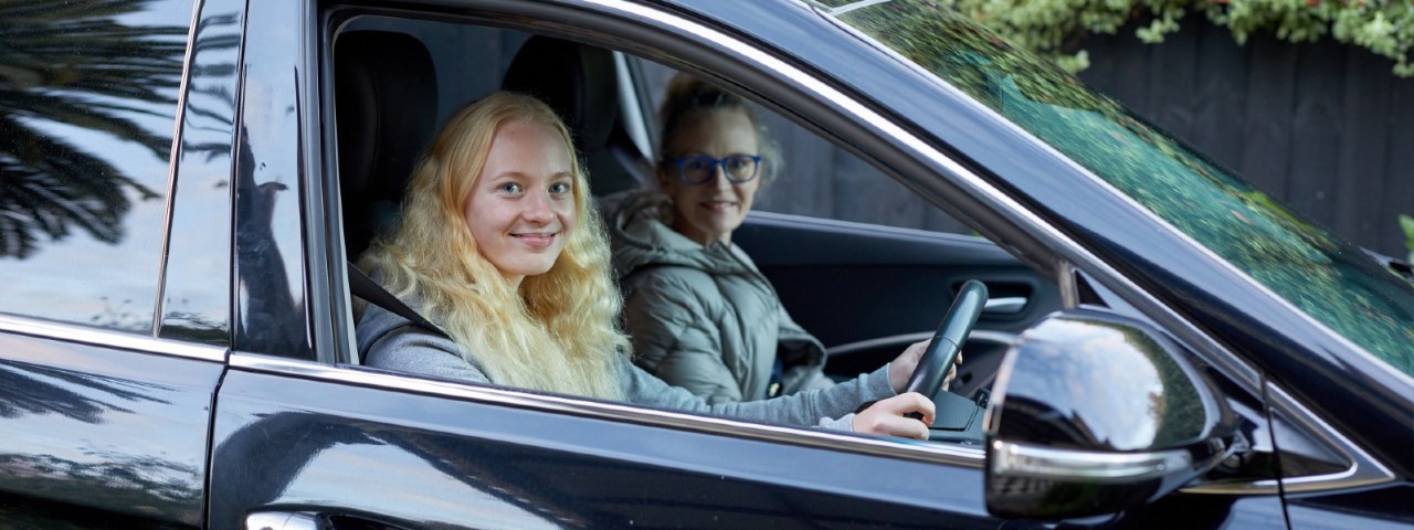 learner driver holding car wheel with her supervisor in passenger seat