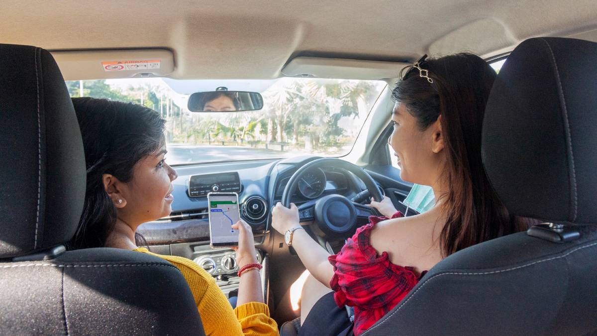 A woman driving a car while her passenger uses a phone to navigate