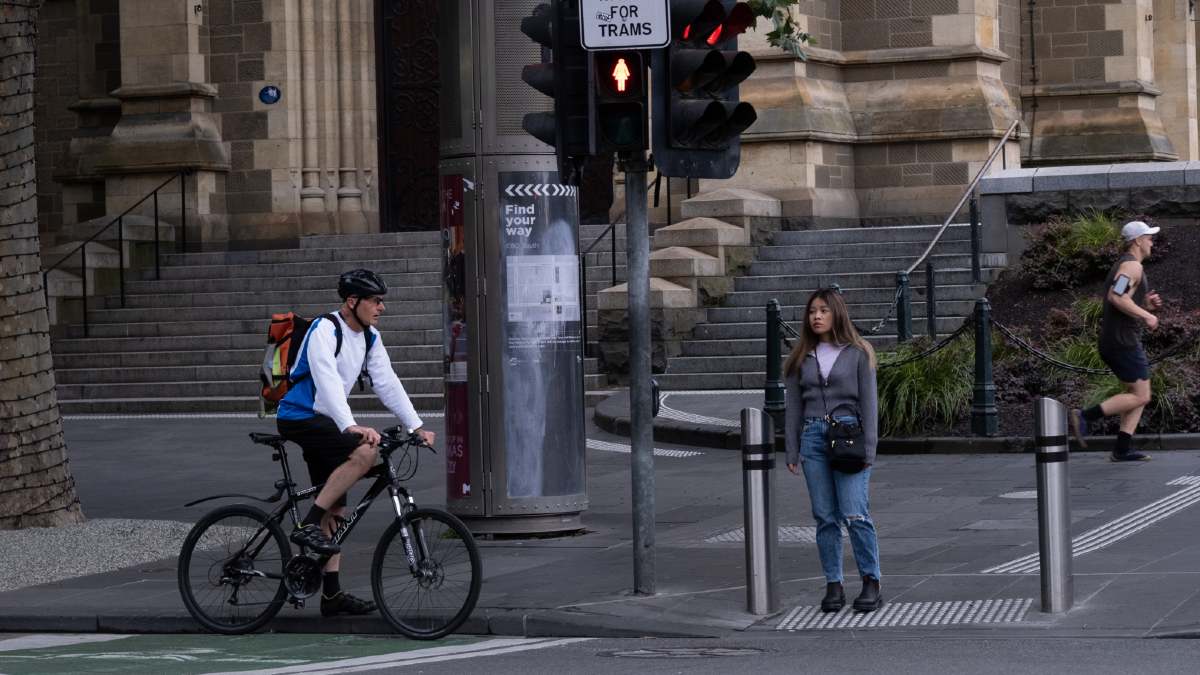 A woman waiting to cross at a pedestrian crossing in Melbourne's CBD. A cyclist waits in the cycle lane