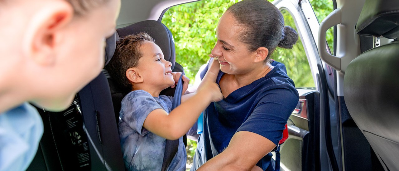 Mother putting son in booster seat using seatbelt.