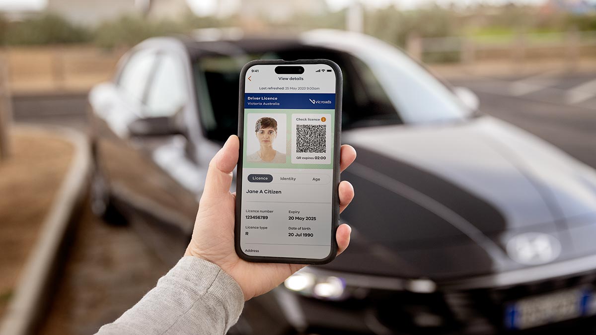 Person on street holding phone in front of car.