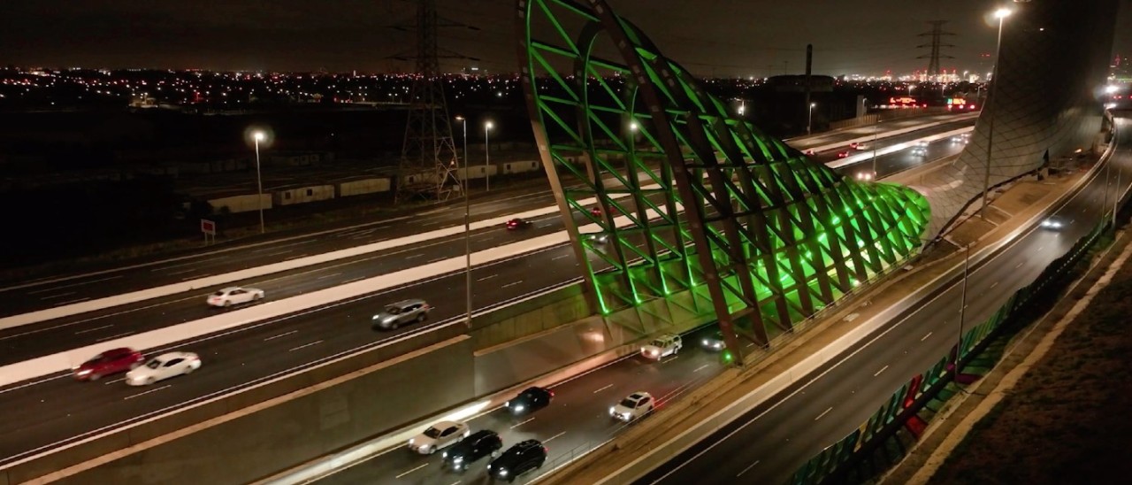 A greenlit West Gate Tunnel exit at nighttime with cars coming out of the tunnel exit