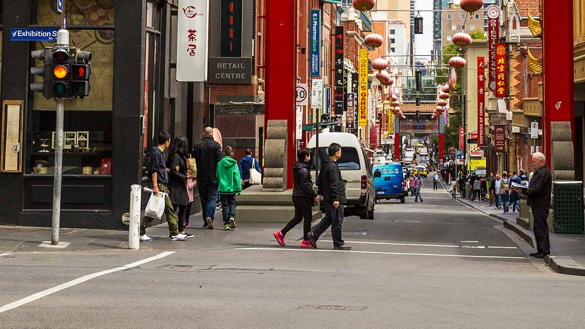 Pedestrians crossing Exhibition Street in Melbourne at entrance to Chinatown as traffic light is yellow
