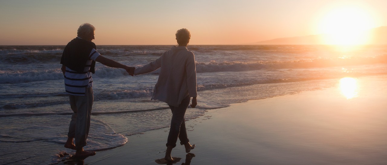Older couple walking barefoot along beach at sunset on the Gold Coast, Australia.